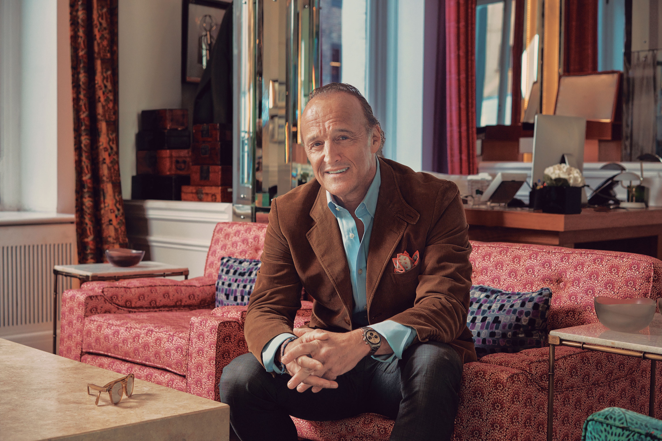 Smiling man sitting on a red patterned sofa in a stylishly decorated room with colorful accents.
