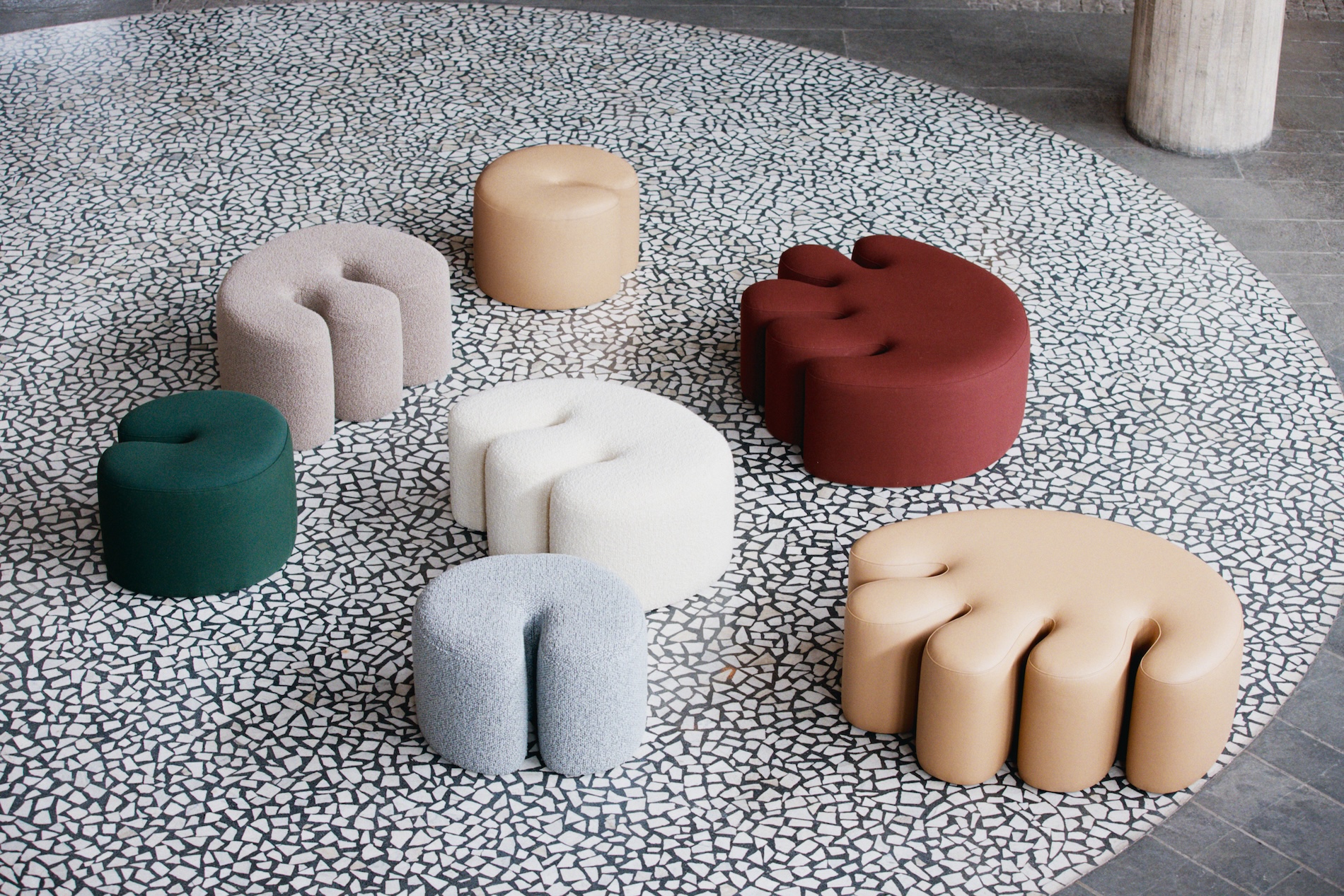 Colorful, uniquely shaped stools arranged in a circular pattern on a speckled, modern flooring surface.