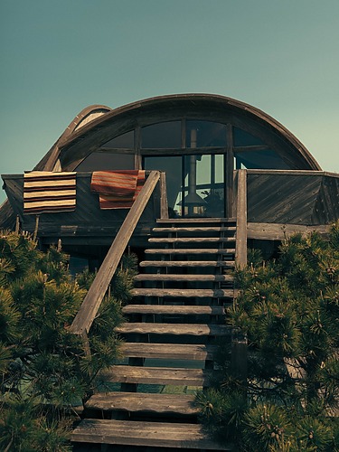 Wooden staircase leading to a round modern house with striped towels and surrounded by green shrubs