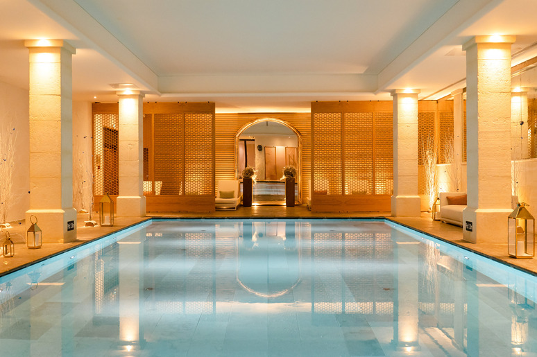 Luxurious indoor swimming pool with elegant lighting and stylish wooden decor panels.
