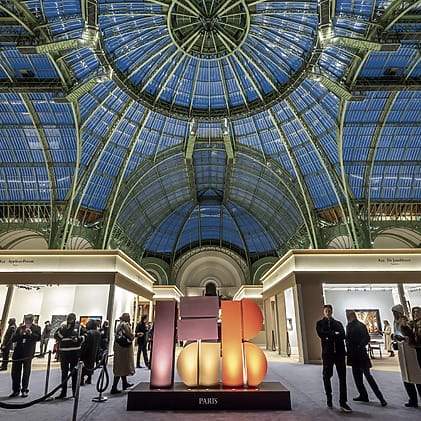 Visitors explore an art exhibit under the grand glass dome of the Grand Palais in Paris, showcasing vibrant illuminated sculptures.