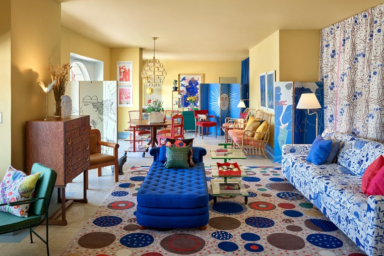 Colorful eclectic living room with patterned furniture, vibrant artwork, and multicolored rug featuring bold geometric designs