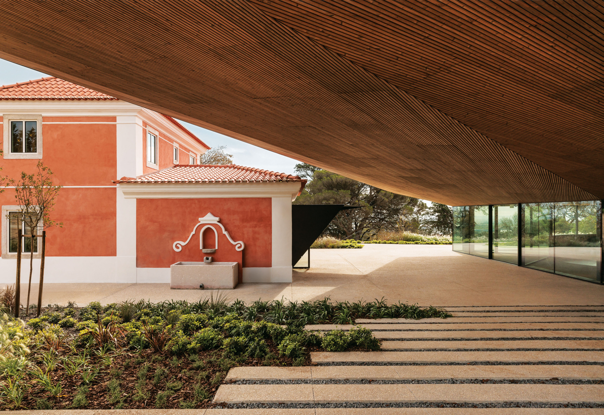 Modern building design with a red and white exterior, wooden ceiling, glass wall, and landscaped steps in the foreground.