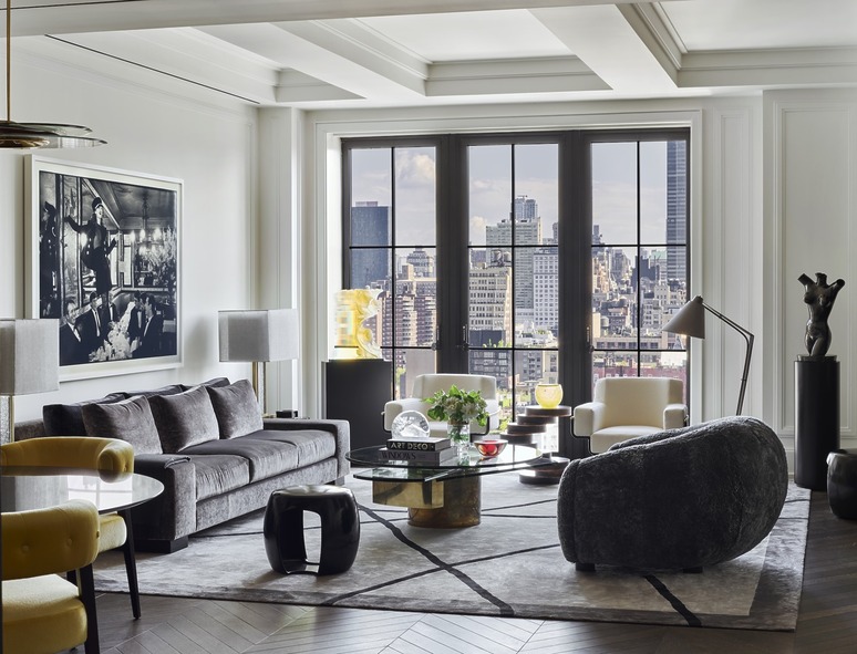 Modern living room with city view, featuring a gray sofa, art pieces, large windows, and contemporary furniture.