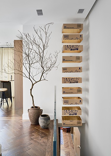 Wall with stacked cereal boxes next to two potted plants on a wooden floor in a modern interior space.