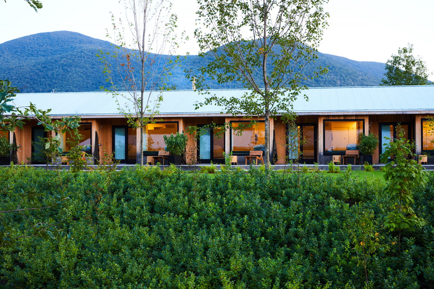 Modern building with large windows surrounded by lush greenery and mountains in the background.