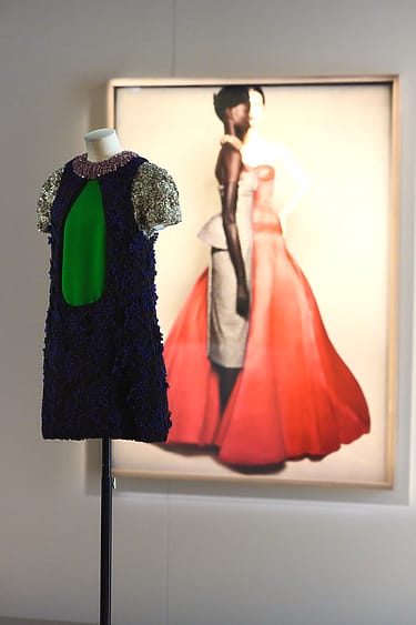 Mannequin displaying a colorful dress with a glamourous backdrop of a woman in a striking red gown in a painting.