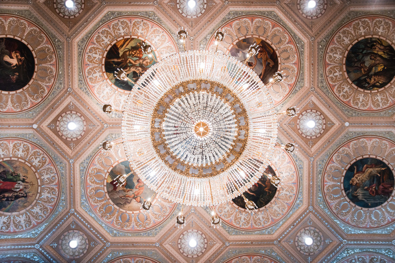 Ornate crystal chandelier hanging from an intricately decorated ceiling with circular paintings and detailed patterns.