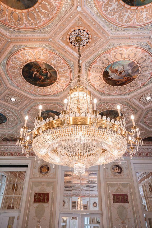 Elegant crystal chandelier hanging in an ornate room with detailed ceiling decorations and classic architectural features