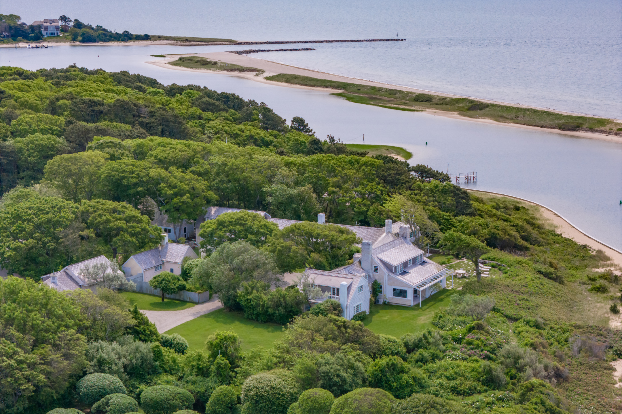 Aerial view of a large coastal house surrounded by greenery and water near a beach.