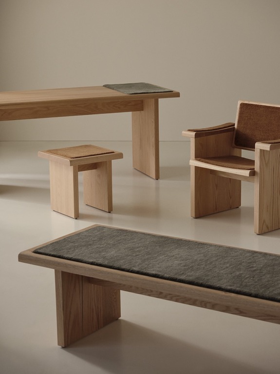 Minimalist wooden furniture set featuring a chair, benches, and a small table with cushions in a neutral-toned room.