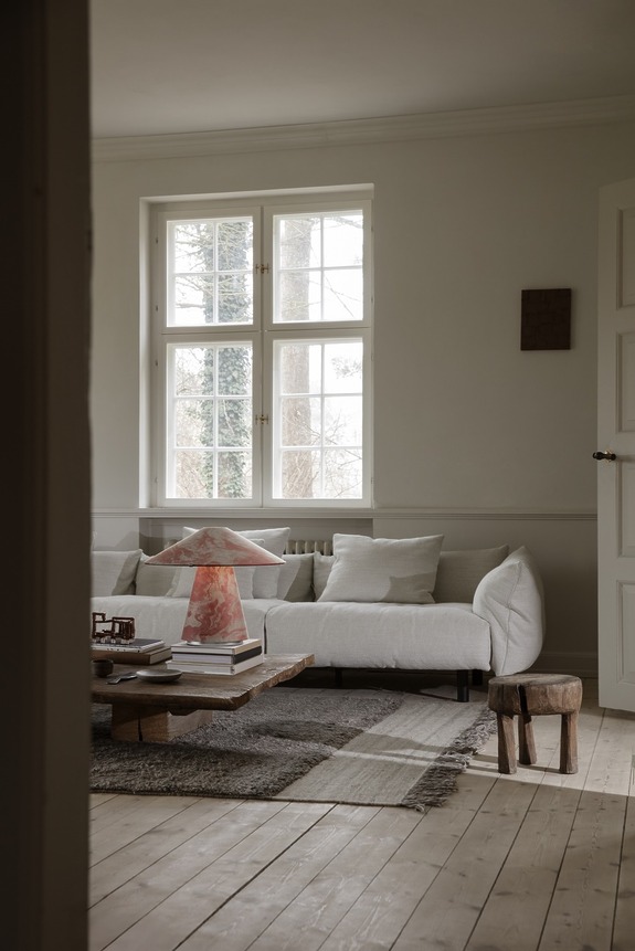 Cozy living room with a white sofa, wooden coffee table, and a small stool on hardwood floors near a large window.