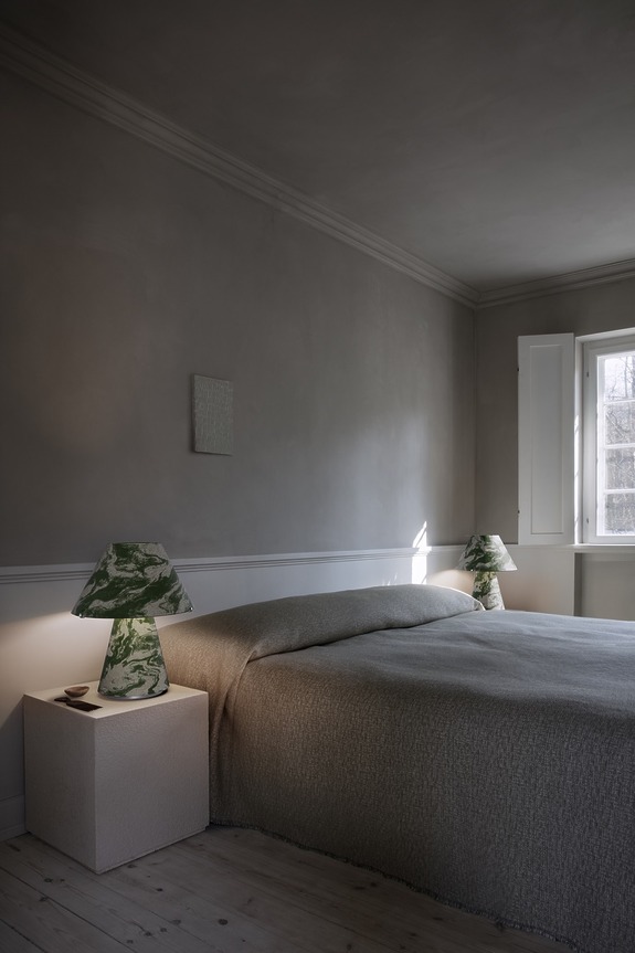 Minimalist bedroom with gray walls, a large bed, and green marble lamps on side tables near a window.
