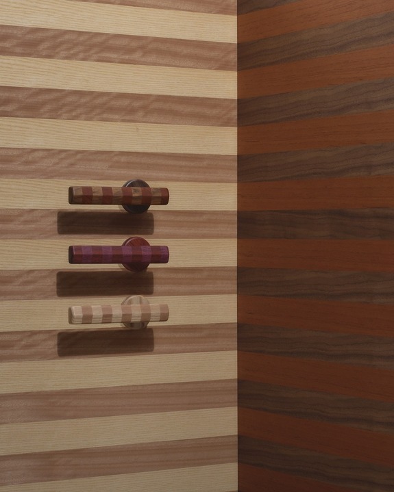 Multicolored striped wooden wall with three matching cylindrical door handles vertically aligned.