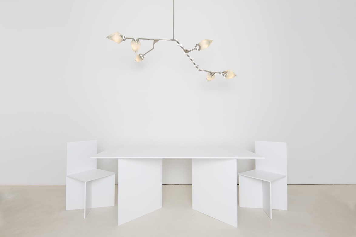 Modern white table and two chairs in minimalist room with unique tree-branch inspired ceiling light fixture.
