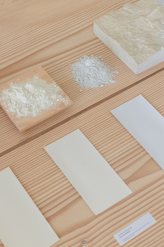 Materials for paper production displayed on a wooden table, including raw powders and texture samples.
