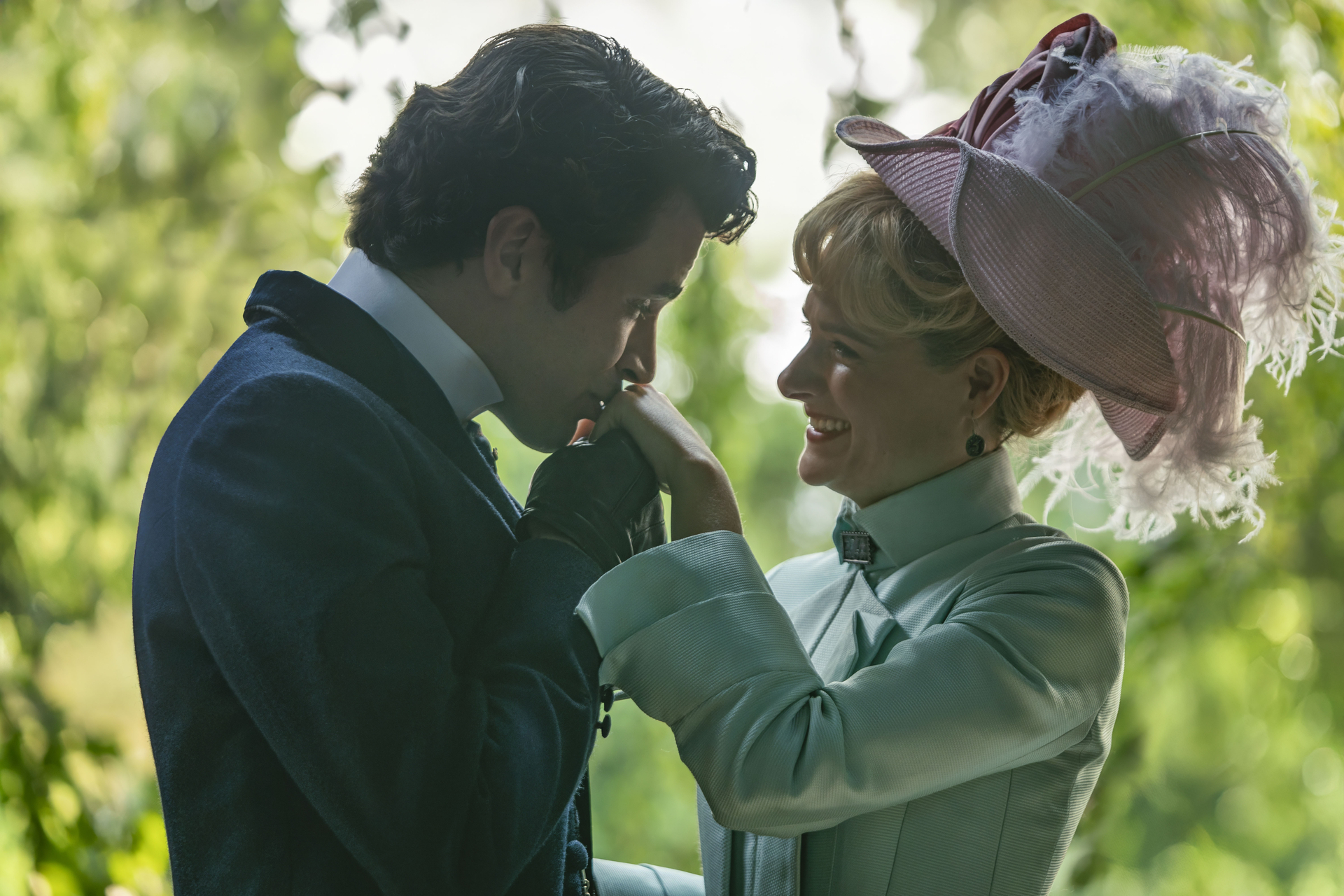 Victorian-era couple in elegant attire, man kissing woman's hand, lush greenery in background.
