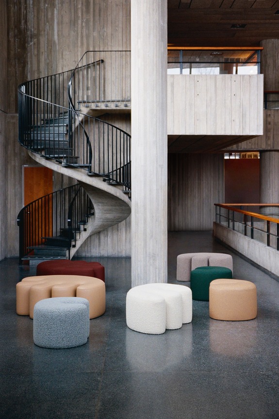 Modern interior with a spiral staircase and various colorful, round upholstered stools on a polished concrete floor.