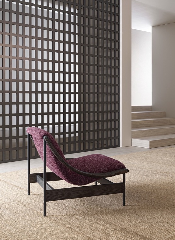 Modern chair with burgundy cushion on a woven carpet in a room with grid-patterned wall and minimalist decor