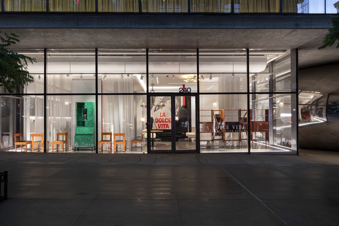 Street view of a modern store with large glass windows displaying chairs and decor items, subtly lit at night.