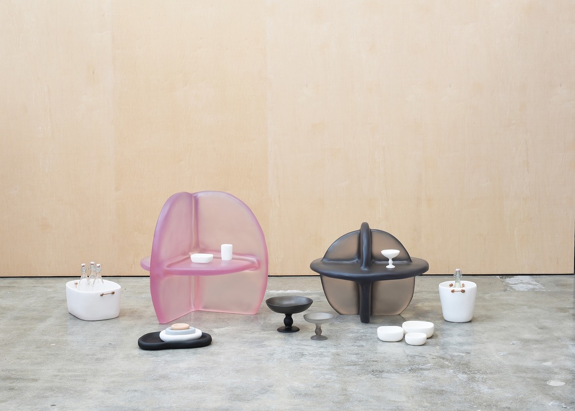 Modern art installation with pink and black translucent chairs, ceramic pottery, and minimalist decor on concrete floor.