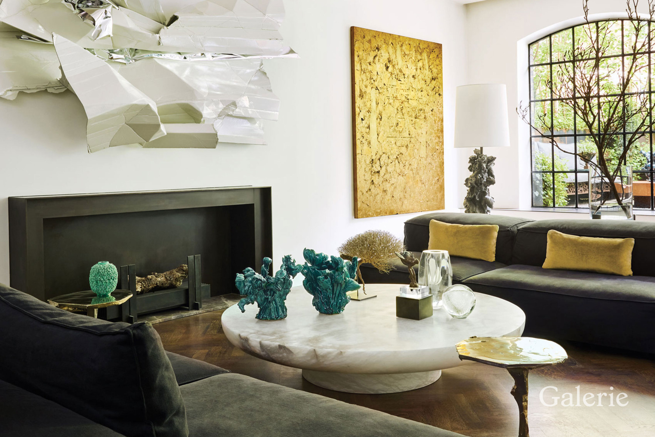 Modern living room with abstract art, dark couches, and a round marble coffee table adorned with decorative sculptures.