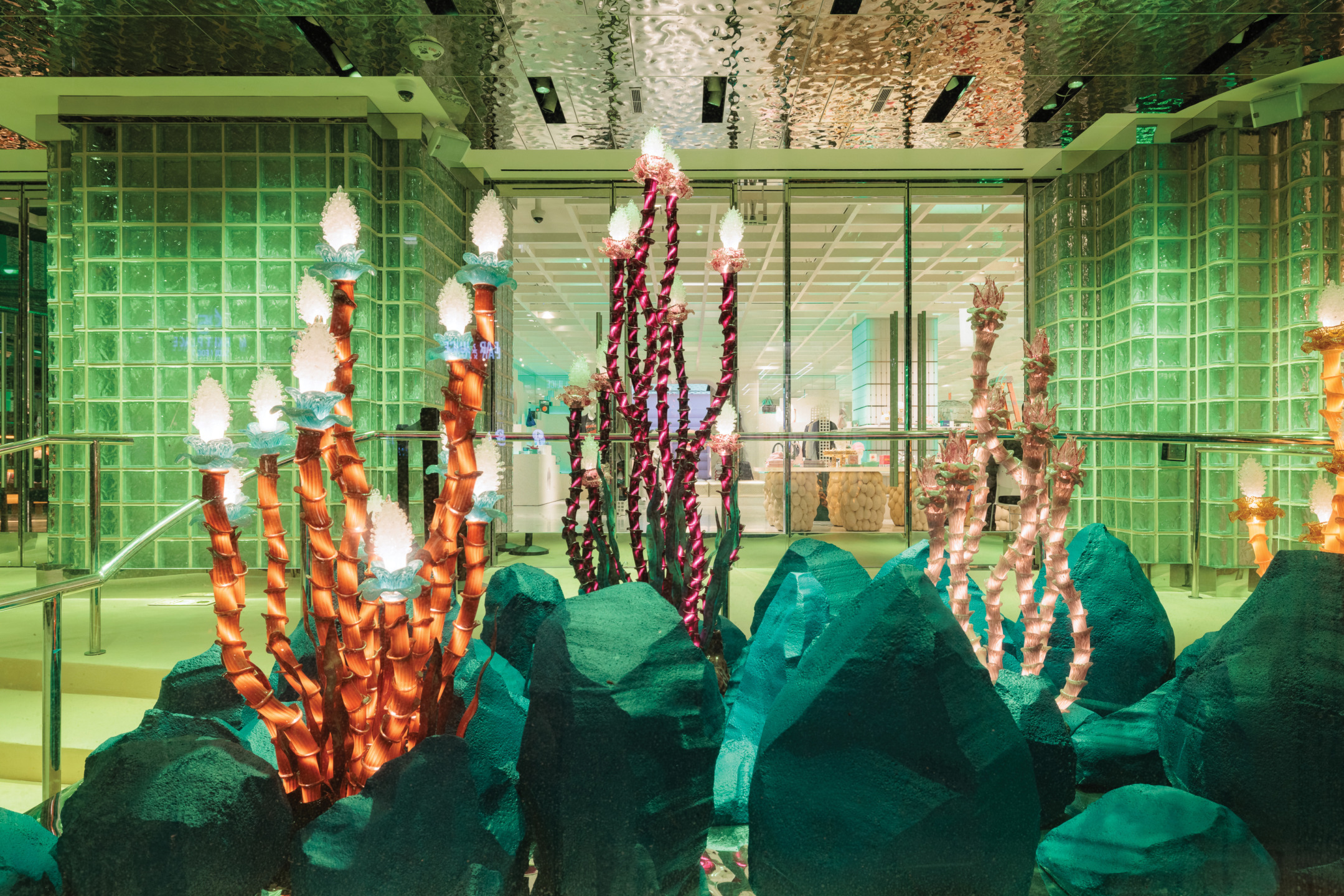 Colorful coral-like sculptures with lights in a modern indoor setting with glass architecture and green accents.