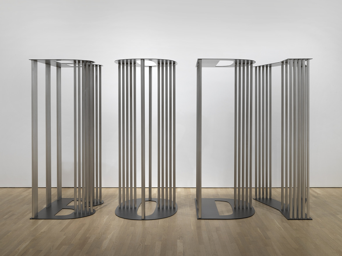 Contemporary metal art installation with vertical bars on a wooden floor in a gallery setting.