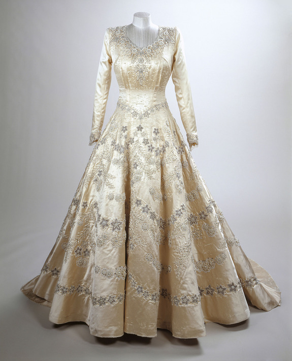 Vintage long-sleeve ball gown with intricate silver embroidery displayed on a mannequin against a plain background.