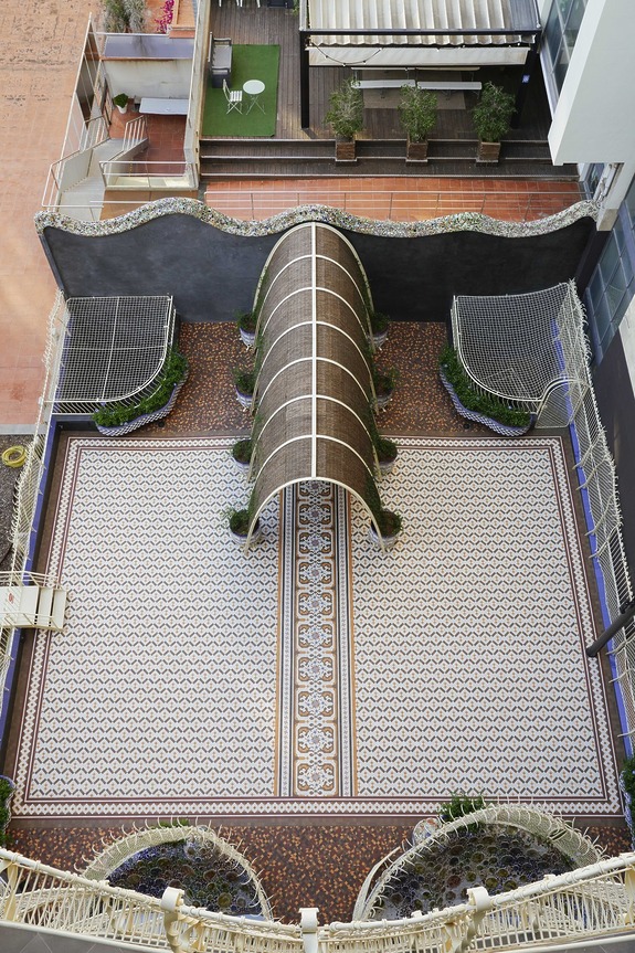 Overhead view of a patterned courtyard with a central archway, ornate design, and greenery along the edges.