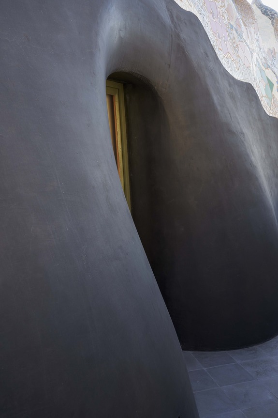 Curved dark wall with a small, partially visible doorway and a colorful wall section in the background.