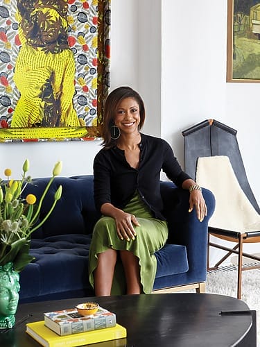 Person seated on blue couch in modern living room with colorful artwork, green skirt, and decorative plants on table.