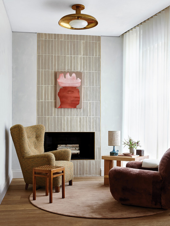 Cozy living room with modern armchairs, a small table, abstract wall art, and a minimalist fireplace under a round ceiling light.
