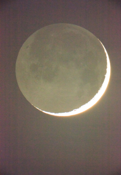 Crescent moon illuminated against a dark night sky, showing detailed surface textures and craters.