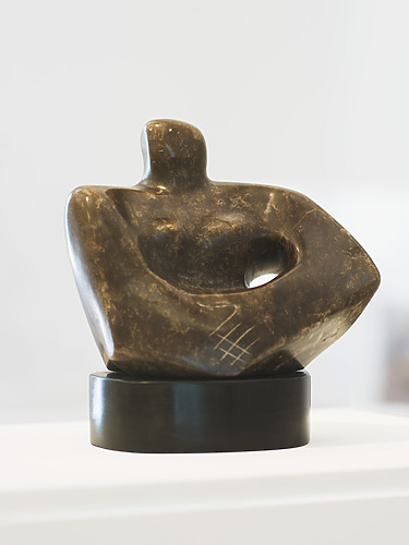Abstract stone sculpture with smooth curves and carved patterns displayed on a round black base in a well-lit setting.