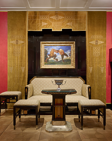 Elegant art deco room with a painting above a vintage sofa, accented by red and gold walls, and two small tables.