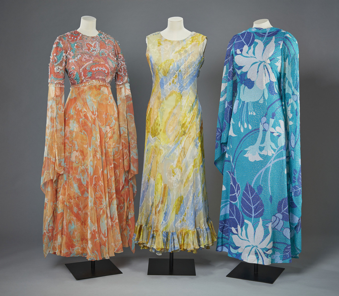 Three vintage mannequin-displayed dresses featuring floral, abstract, and colorful patterns on a neutral background.