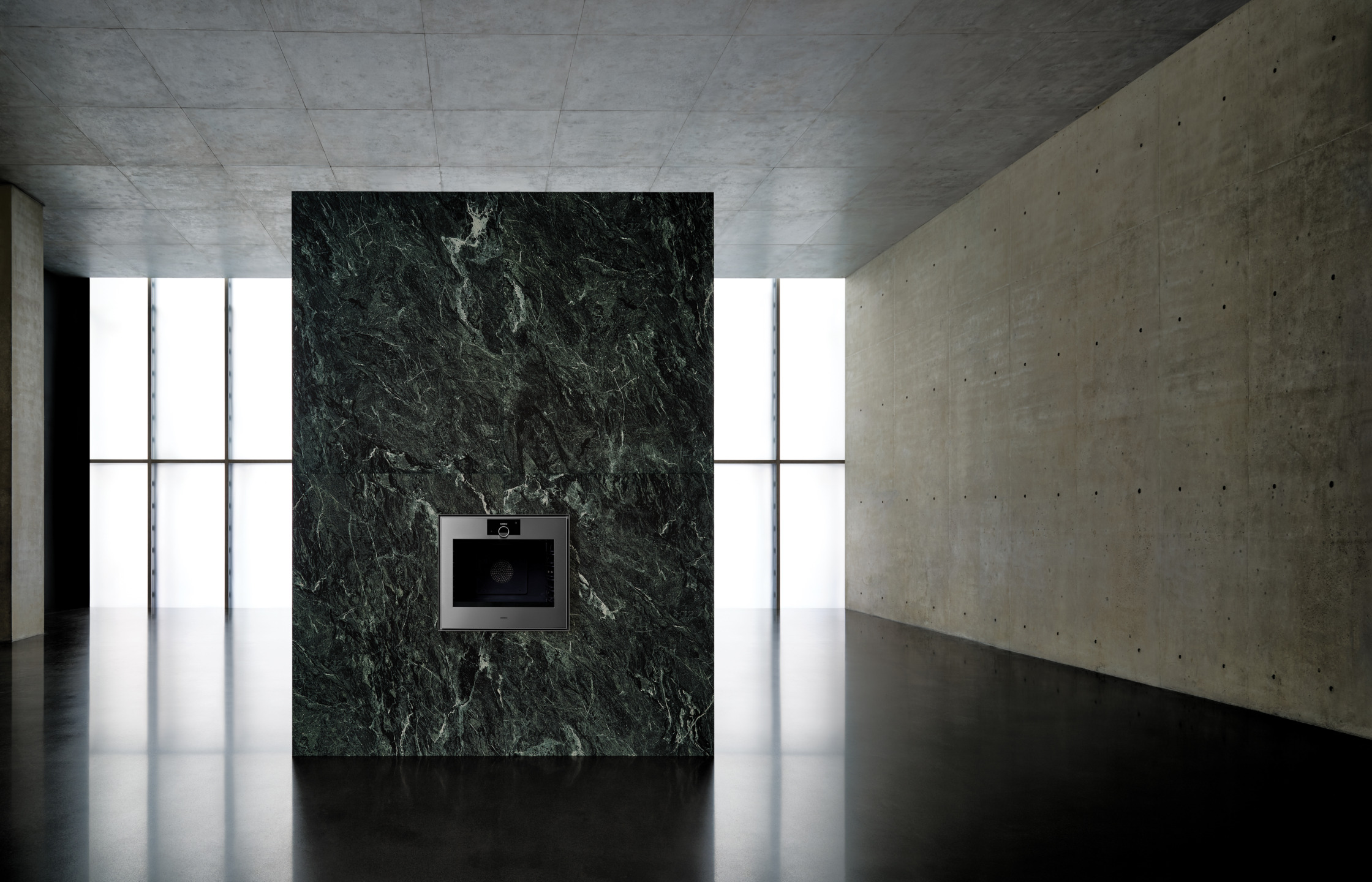 Modern kitchen with a sleek built-in oven set in a dark green marbled island, surrounded by minimalist concrete walls.