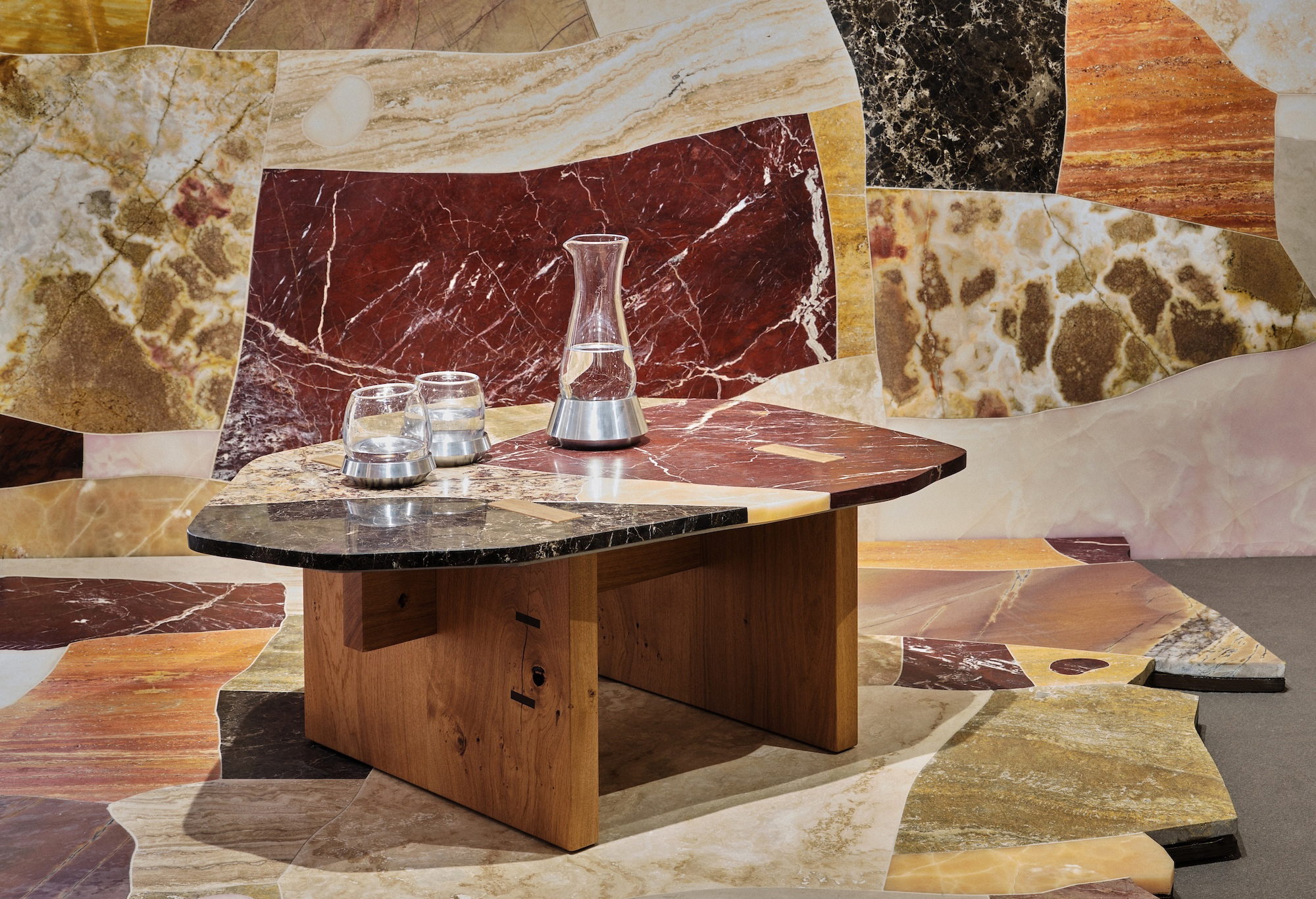 Modern coffee table with angular marble top, glass pitcher and glasses placed on colorful stone tile floor background.