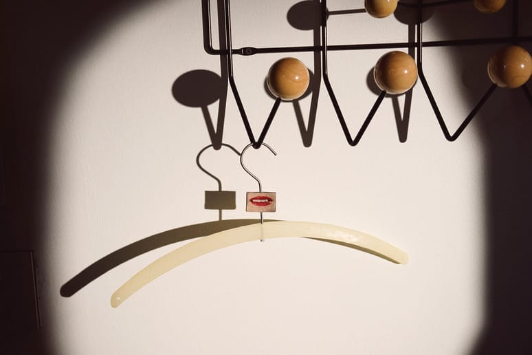 Decorative hanger casting shadow on wall with geometric hook design and wooden knobs, illuminated by soft light.