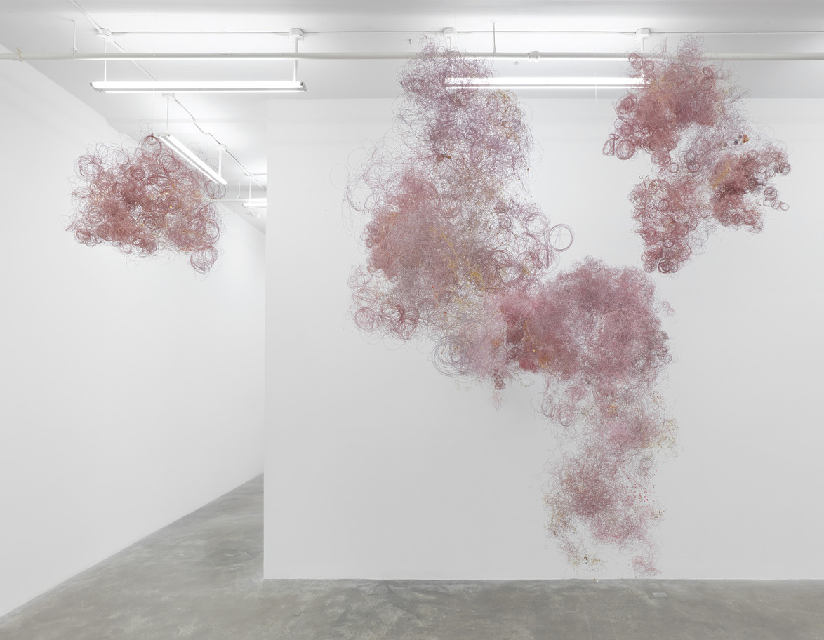 Pink and red wispy wire installations hanging in a white gallery space.
