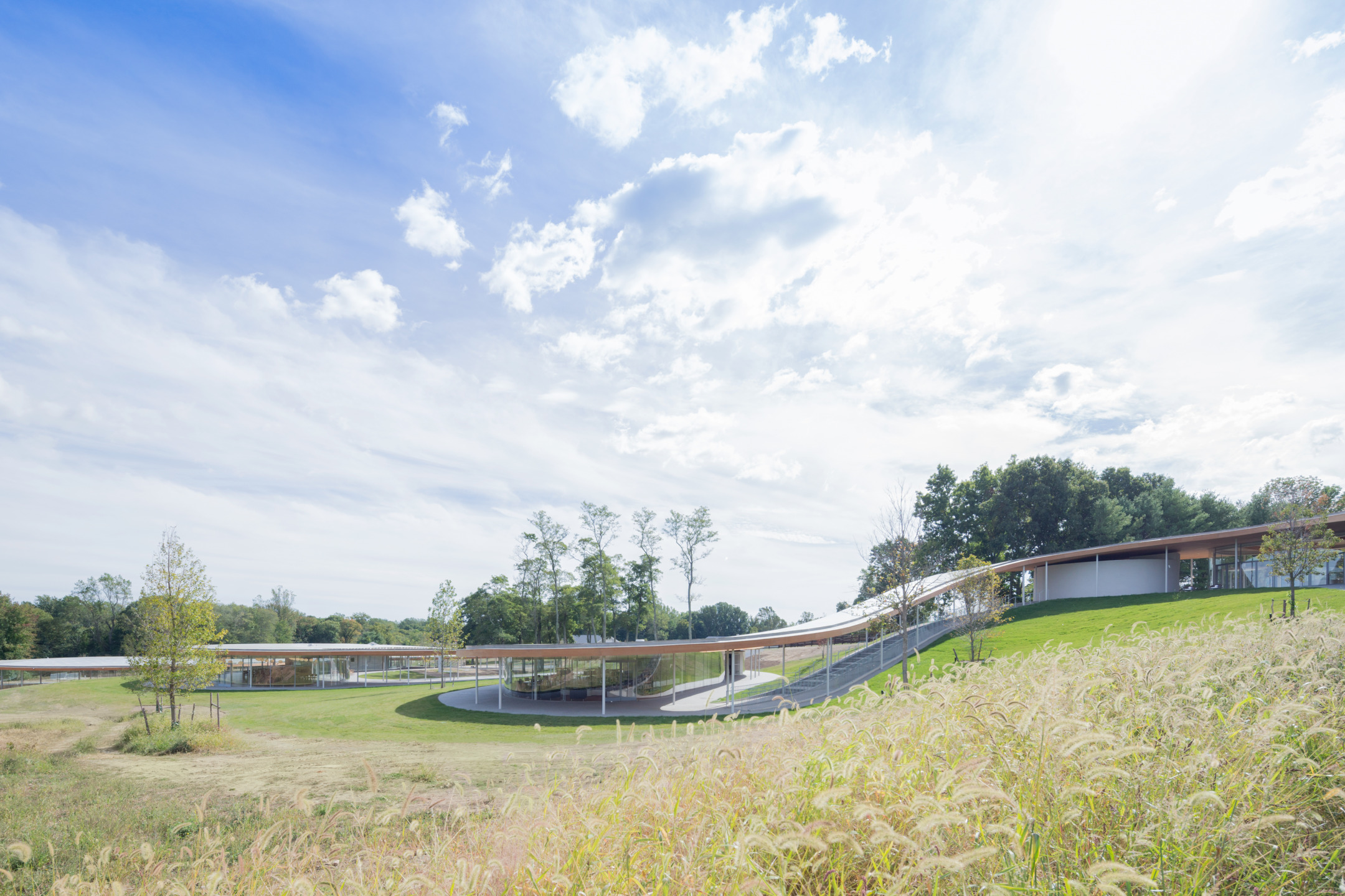 Modern architectural building surrounded by grassy fields under a blue sky with scattered clouds.