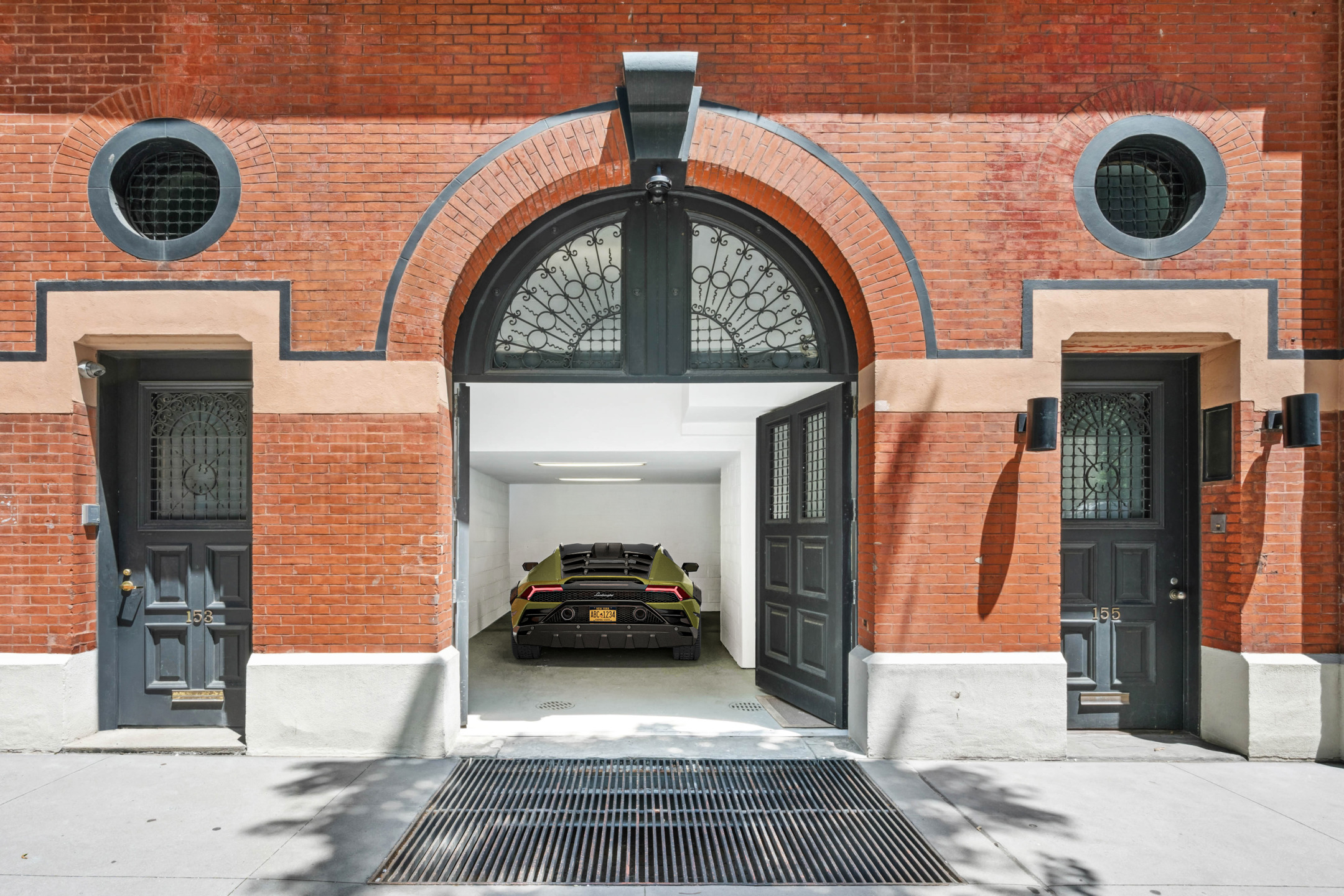 Car parked inside a garage with arched entrance in a brick building, black double doors open revealing modern interior.