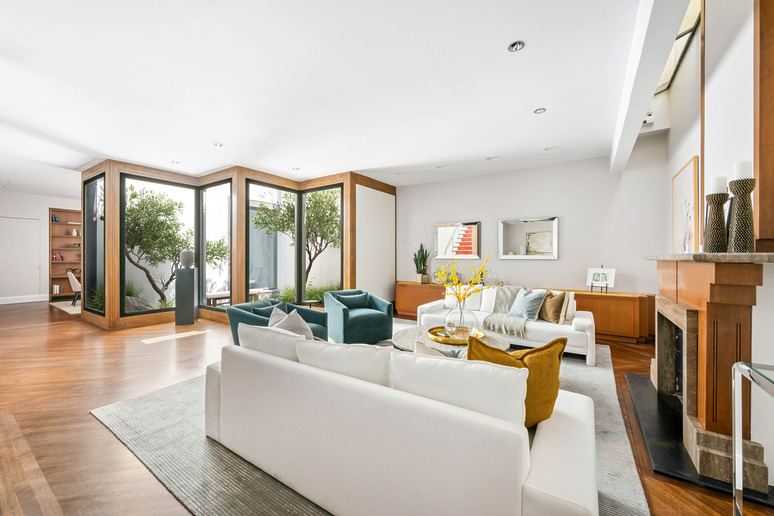 Modern living room with large windows, white couch, green plants, wooden floor, and fireplace.