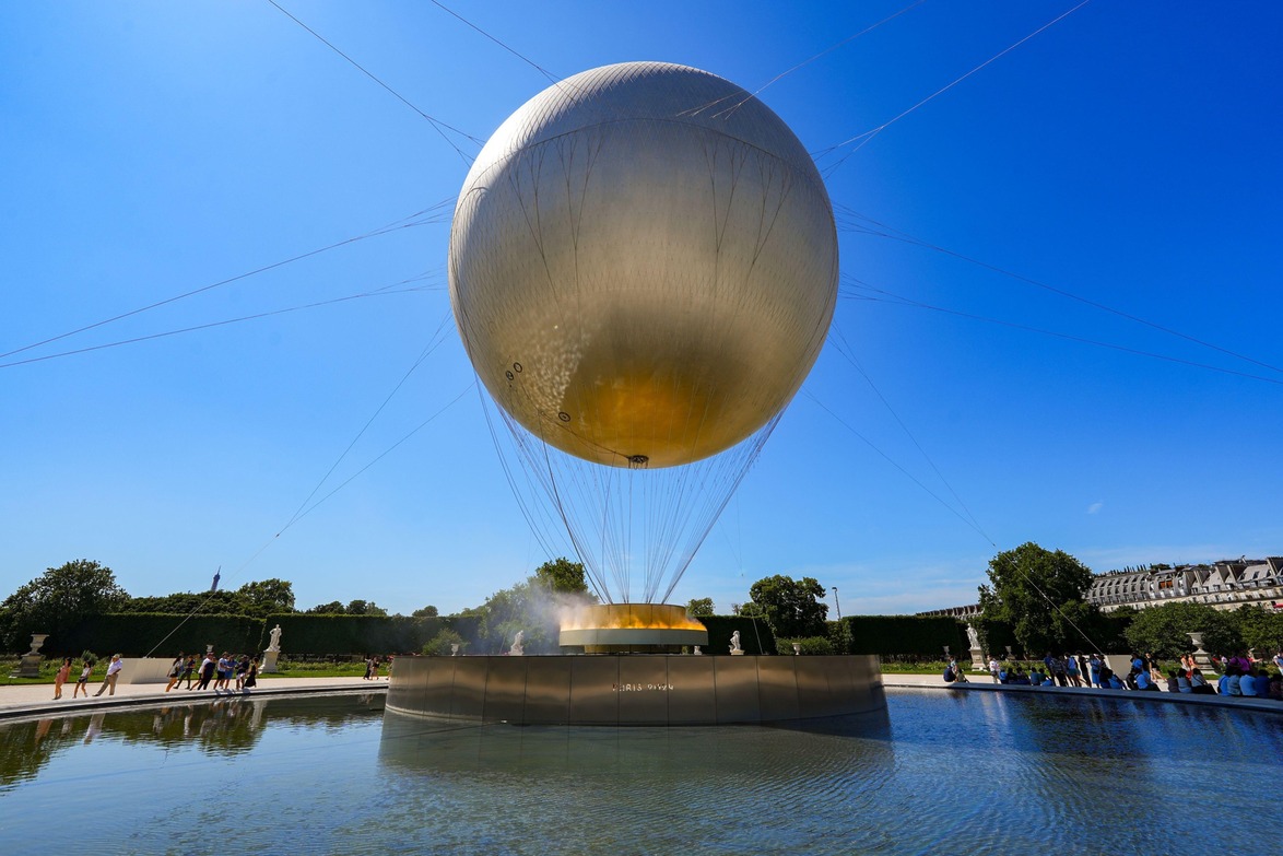 Large spherical balloon hovering over a fountain in a park on a sunny day with trees and people in the background