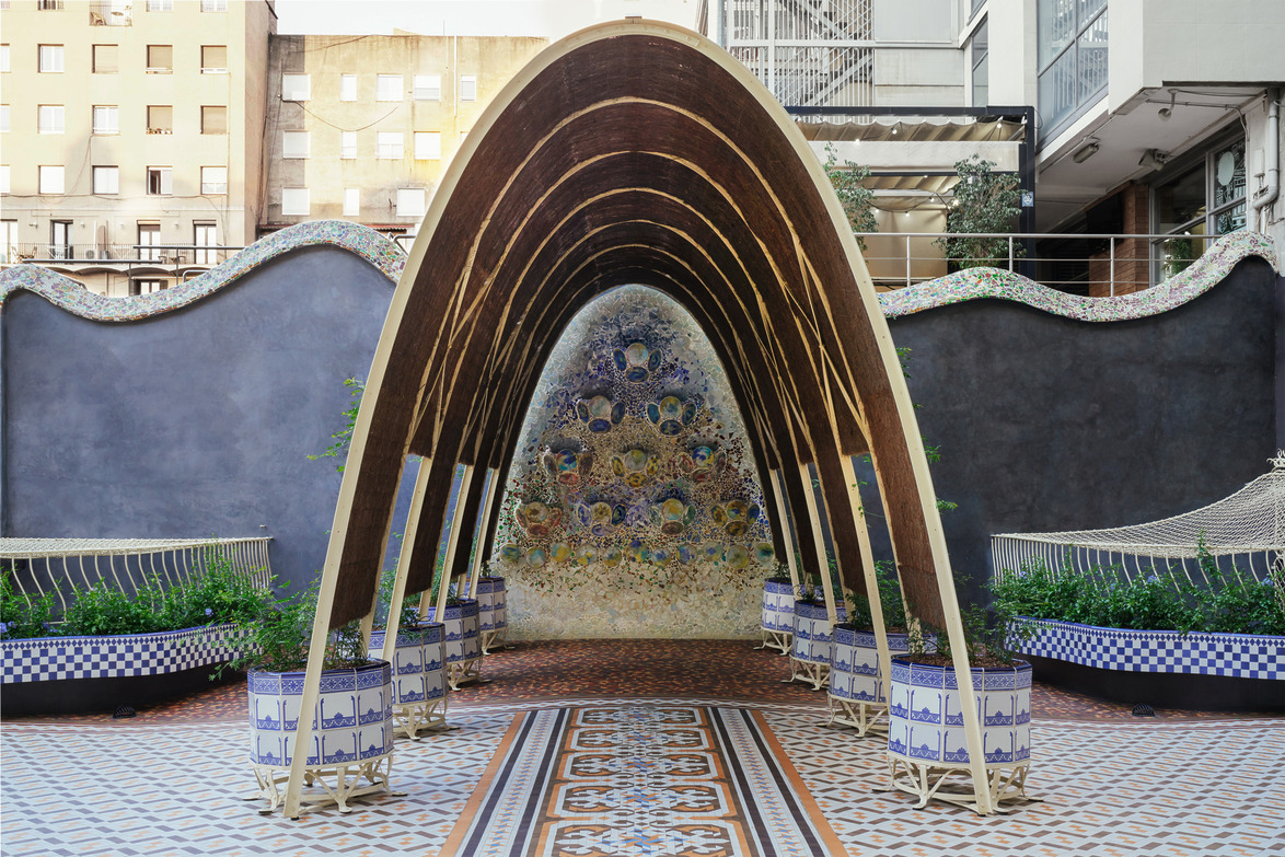 Architectural structure with curved wooden arches in a decorative courtyard featuring intricate tiling and mosaic wall art.