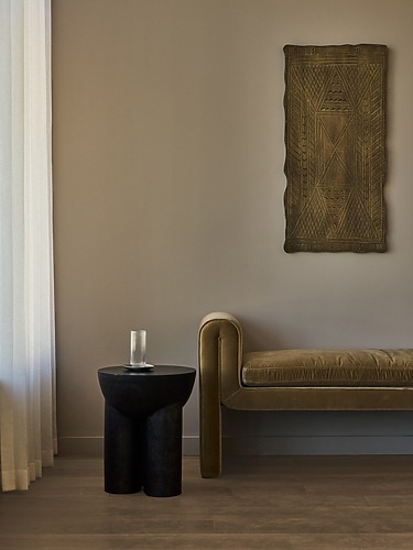 Minimalist room with a velvet bench, black side table, glass of water, and abstract wall art.