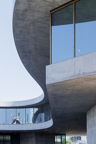 Modern architectural building with curved concrete design and large glass windows reflecting the clear sky.