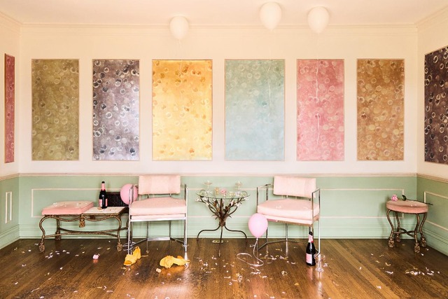 Elegant party aftermath with balloons, champagne bottles, and chairs in a pastel-colored room with abstract art on the walls.
