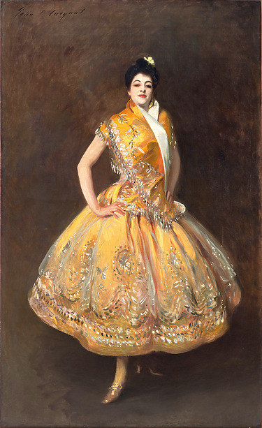 A woman in a vibrant yellow dress poses confidently, showcasing intricate patterns and embellishments, circa early 20th century.